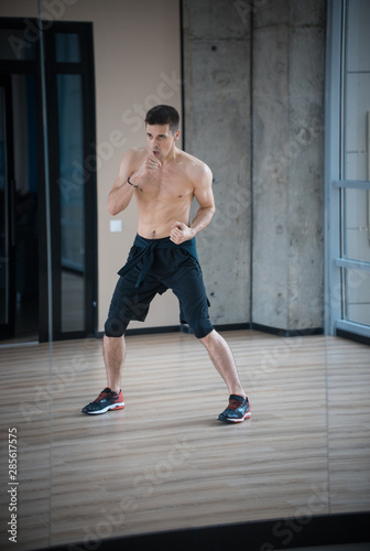 An athletic young man boxer standing in fighting pose in the bright studio