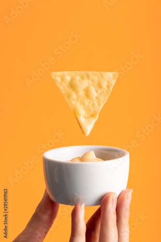 Fotografie cropped view of woman holding cheese sauce in bowl under crispy corn nacho isola