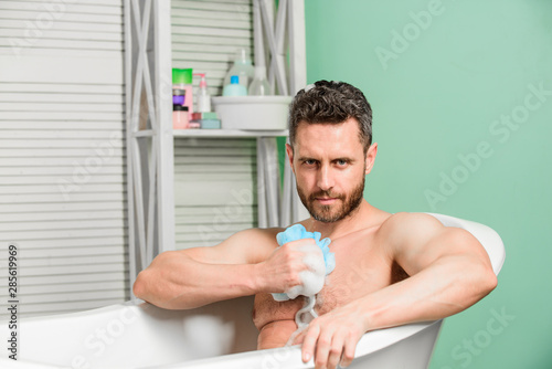 Macho sitting naked in bathtub washing with sponge. hygiene and health. Morning shower. desire and temptation. personal care. Sexy man in bathroom. man wash muscular body with foam sponge © be free