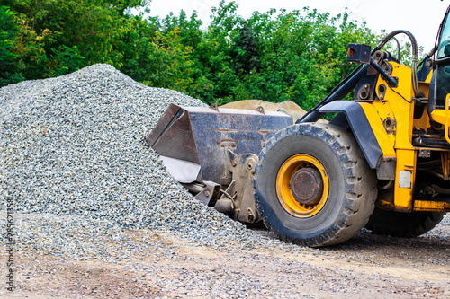Yellow wheel loader bulldozer is working in quarry against the background of crushed stone storage.