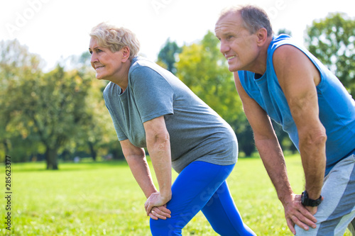 Active flexible senior couple stretching leg in park on sunny day