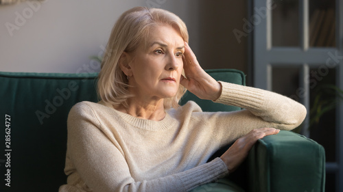 Pensive middle aged lady looking away sit alone at home photo