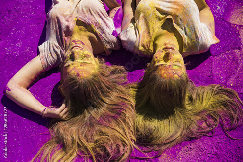 Two young women lying on purple holi color powder