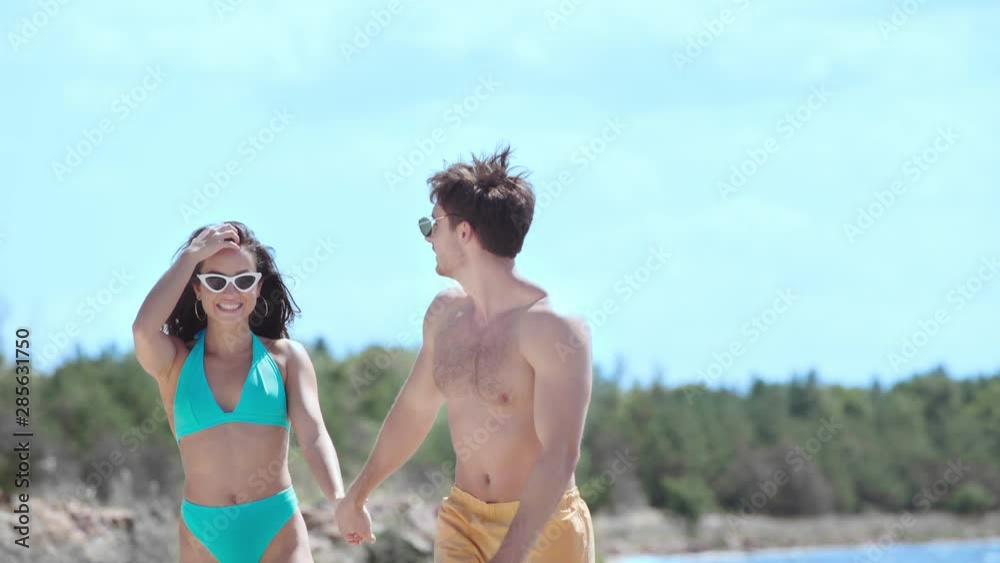 happy young couple holding hands and talking while walking on seaside happy young couple holding hands and talking while walking on seaside