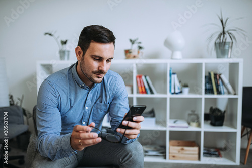 Casual man using phone in modern bright living room.