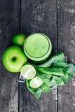 Green apple smoothie in glass and kale leaves on wooden table