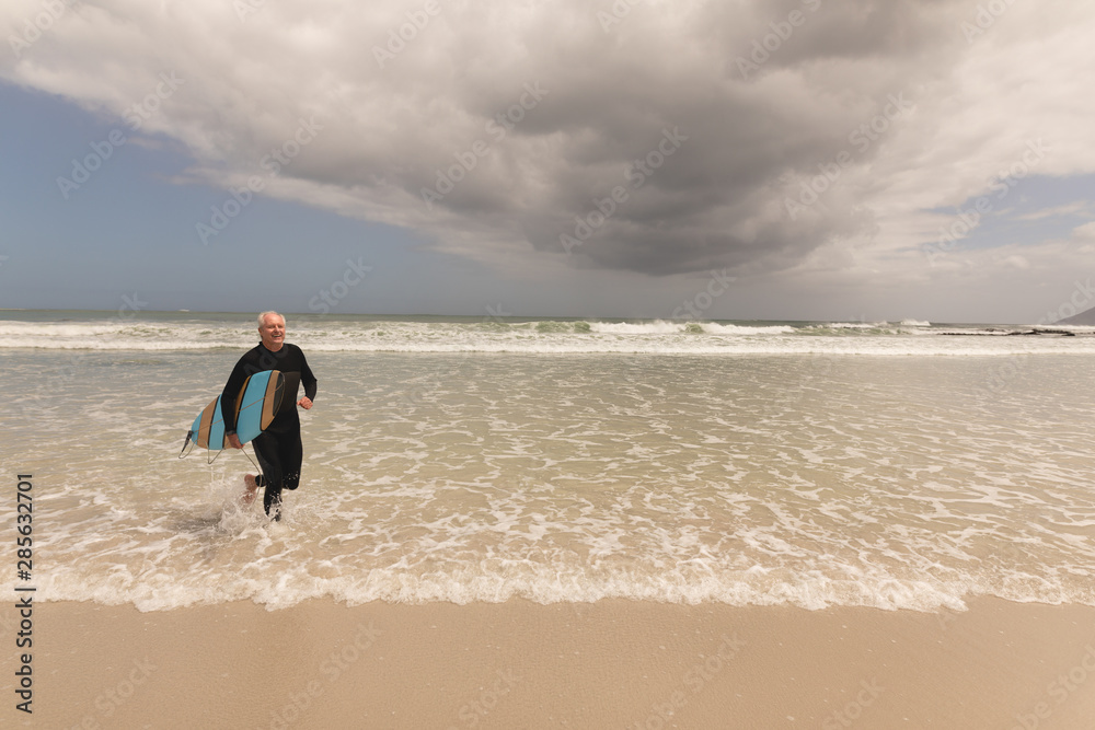 Senior man running with surfboard on the beach