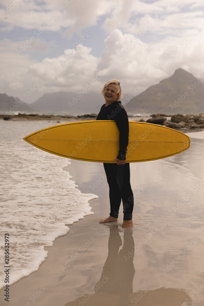 Senior woman standing with surfboard on the beach