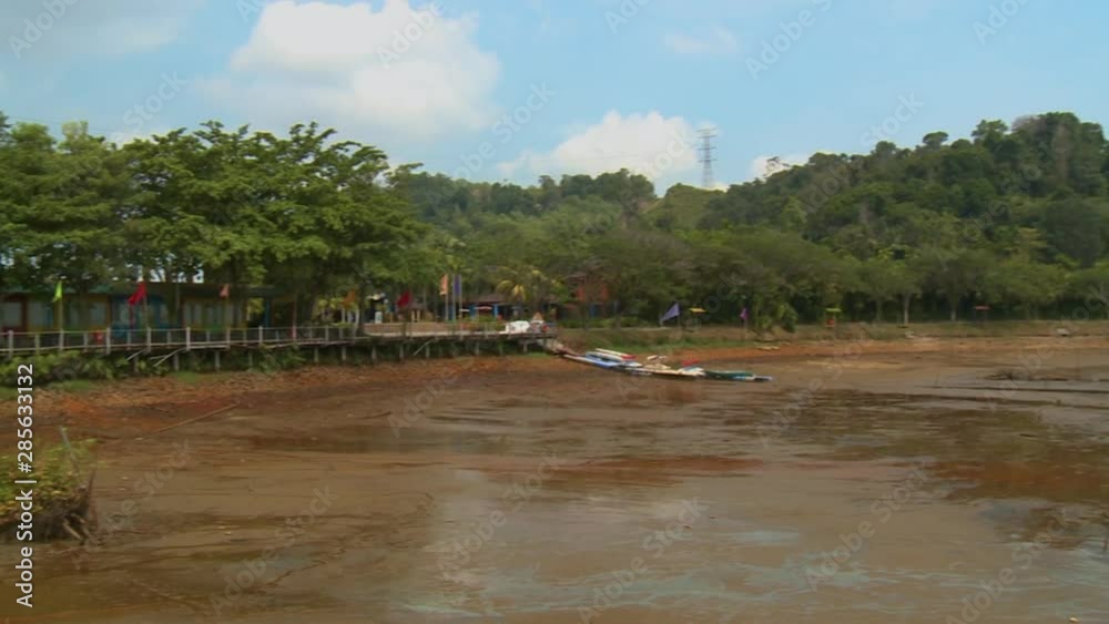Wide low-angle panning shot of receded water level, stilt walking path with coloured flag posts, and tropical rainforest trees, Bukit Merah Lake town, Malaysia Wide low-angle panning shot of receded water level, stilt walking path with coloured flag posts, and tropical rainforest trees, Bukit Merah Lake town, Malaysia