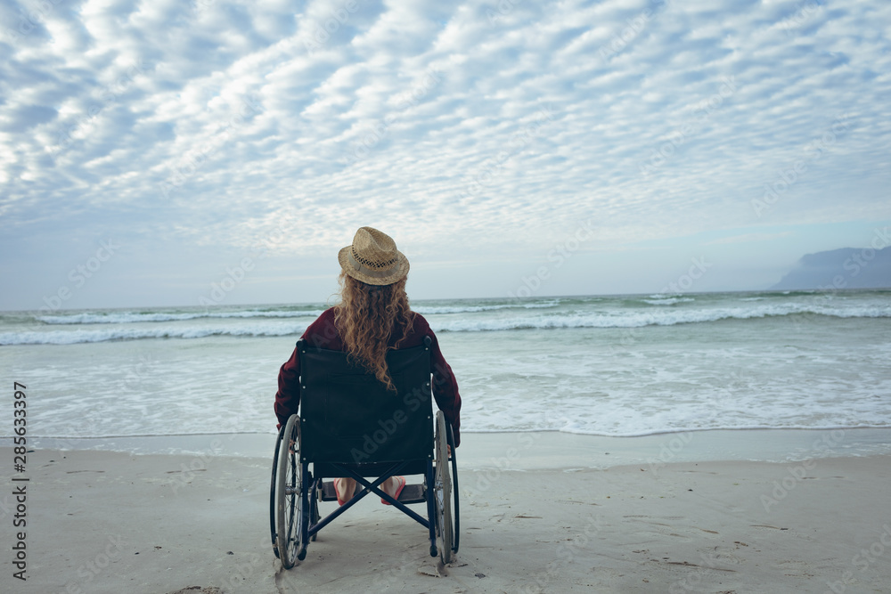 Disabled woman sitting on wheelchair at beach  - obrazy, fototapety, plakaty 