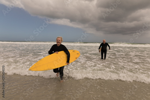 Senior couple running with surfboard on the beach
