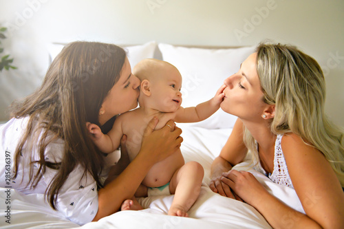 Canvas Print Two lesbian mother and baby on bed having fun