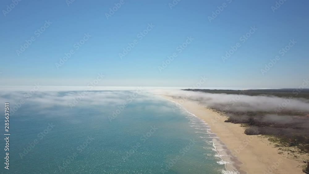 Scenic panoramic aerial drone view of low fog clouds over turquoise ocean and beach along coastal landscape in Western Australia, with blue sky, sunshine and horizon on a summer sunny day. Scenic panoramic aerial drone view of low fog clouds over turquoise ocean and beach along coastal landscape in Western Australia, with blue sky, sunshine and horizon on a summer sunny day.