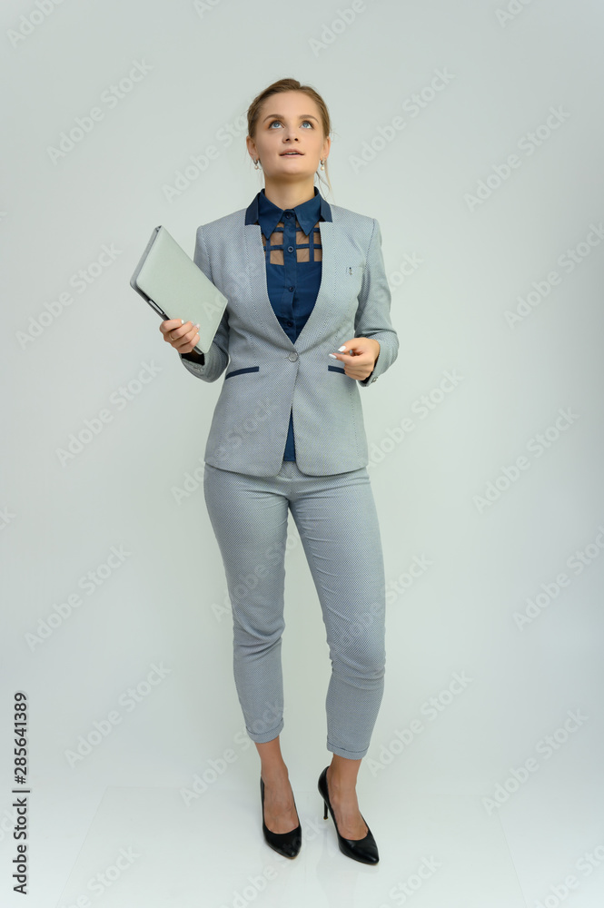 Full length studio portrait of a pretty young woman girl in a business suit on a white background with a folder in hands. He stands right in front of the camera, explains, with emotion. Full length studio portrait of a pretty young woman girl in a business suit on a white background with a folder in hands. He stands right in front of the camera, explains, with emotion.