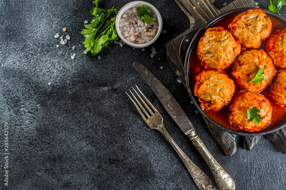 Homemade chicken meatballs in tomato sauce in a frying pan on dark stone or concrete table. Top view copy space