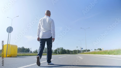 Rear view of a bald man walking along еmpty the road. Full shot.