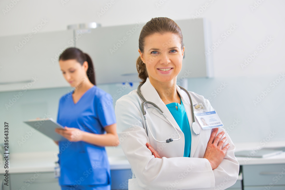 Portrait of confident doctor standing against nurse at clinic Portrait of confident doctor standing against nurse at clinic