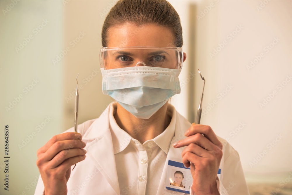 Portrait of confident dentist wearing surgical mask and eyewear while holding dental equipments