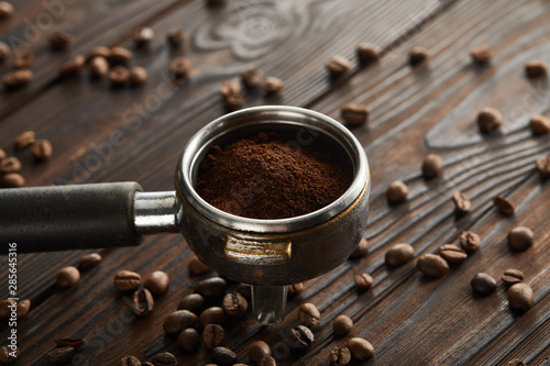 Portafilter filled with fresh ground coffee on dark wooden surface with coffee beans