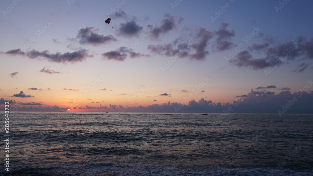 Parasailing in blue sea during orange evening sundown on horizon, beautiful scenery of tranquil seascape in summer evening twilights. Tourists on a parachute over the sea. Sunset paradise Parasailing in blue sea during orange evening sundown on horizon, beautiful scenery of tranquil seascape in summer evening twilights. Tourists on a parachute over the sea. Sunset paradise