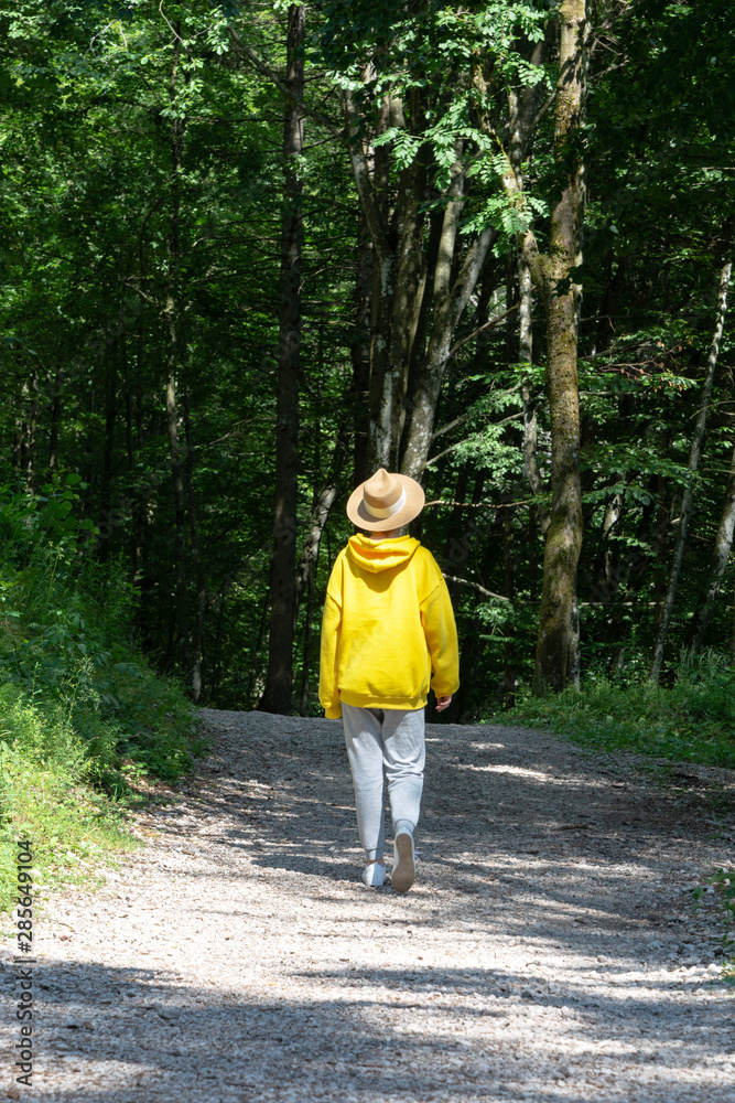 A girl in a bright yellow hoodie with a hat is walking along a path in the forest. A girl in a bright yellow hoodie with a hat is walking along a path in the forest.