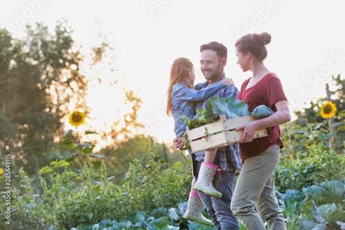 Portrait of a family of famers carrying their vegetables home in wooden boxes, at the end of the day, the Father is carrying their daughter