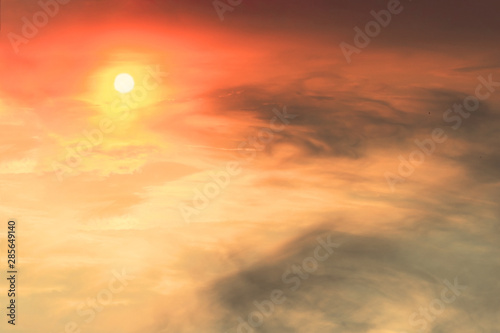 The sunset in the sky is red-orange with gray clouds in the form of stains on which the sun shines.