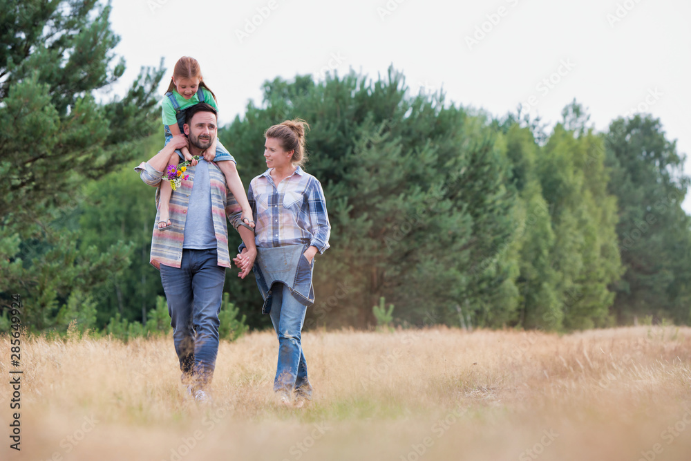 Fototapeta premium Young Caucasian family walking across field with young girl holding bouquet of flowers, concept organic ecologically friendly family