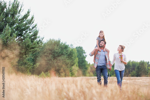 Young Caucasian family walking across field with young child on her fathers shoulders with the wife holding a bouquet of flowers
