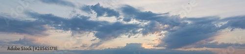 Panorama of the cloudy sky illuminated by the rays of the setting sun