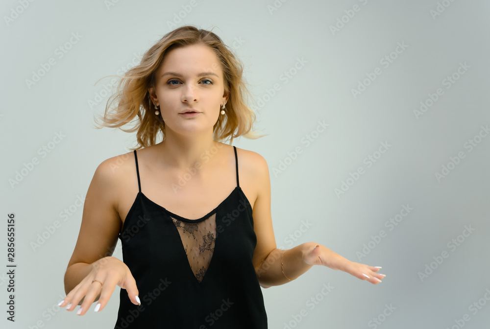 Photo studio portrait of a cute blonde young woman girl in a black blouse on a white background. He stands right in front of the camera, explains with emotion. Photo studio portrait of a cute blonde young woman girl in a black blouse on a white background. He stands right in front of the camera, explains with emotion.