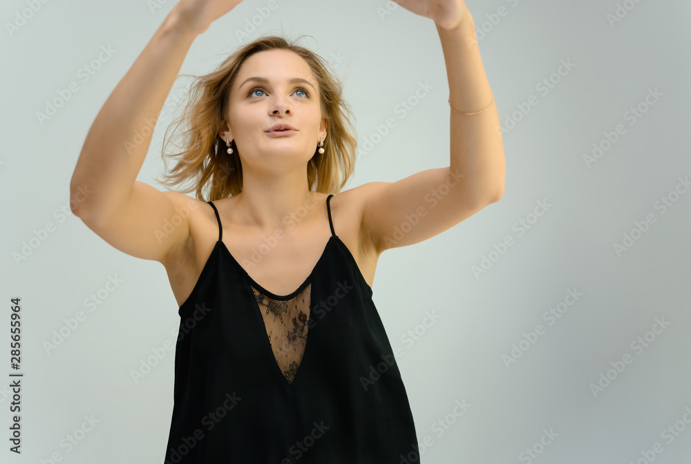 Photo studio portrait of a cute blonde young woman girl in a black blouse on a white background. He stands right in front of the camera, explains with emotion.