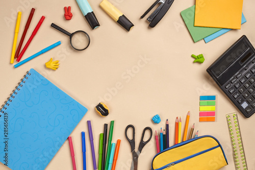 Flat lay photo of workspace desk with school accessories or office supplies on pink background.