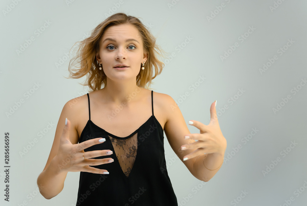 Photo studio portrait of a cute blonde young woman girl in a black blouse on a white background. He stands right in front of the camera, explains with emotion. Photo studio portrait of a cute blonde young woman girl in a black blouse on a white background. He stands right in front of the camera, explains with emotion.