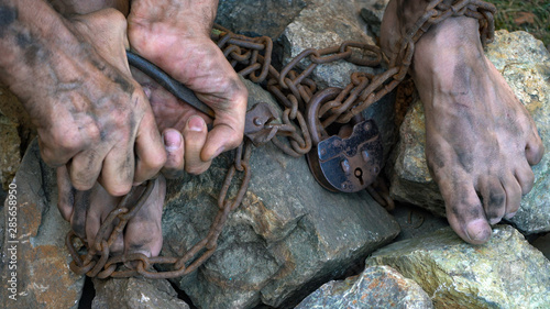 Hands and feet of a slave entangled in iron chains. An attempt to break free from slavery. The symbol of slave labor. Hands in chains.