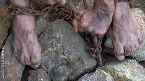 Hands and feet of a slave entangled in iron chains. An attempt to break free from slavery. The symbol of slave labor. Hands in chains photo