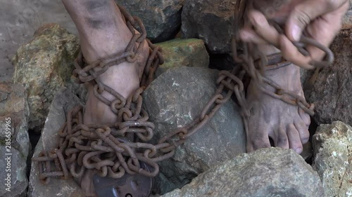 Hands and feet of a slave entangled in iron chains. An attempt to break free from slavery. The symbol of slave labor. Hands in chains. photo