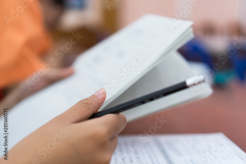 student taking notes lecture in high school or university with holding pencil writing on paperwork sheet and taking final exam in examination classroom