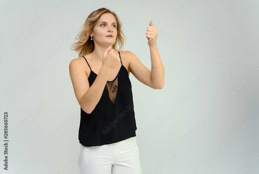 Photo studio portrait of a cute blonde young woman girl in a black blouse and white pants on a white background. He stands right in front of the camera, explains with emotion. Photo studio portrait of a cute blonde young woman girl in a black blouse and white pants on a white background. He stands right in front of the camera, explains with emotion.