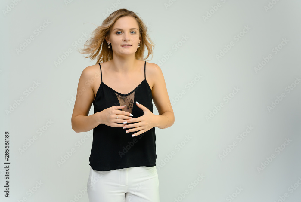 Photo studio portrait of a cute blonde young woman girl in a black blouse and white pants on a white background. He stands right in front of the camera, explains with emotion. Photo studio portrait of a cute blonde young woman girl in a black blouse and white pants on a white background. He stands right in front of the camera, explains with emotion.