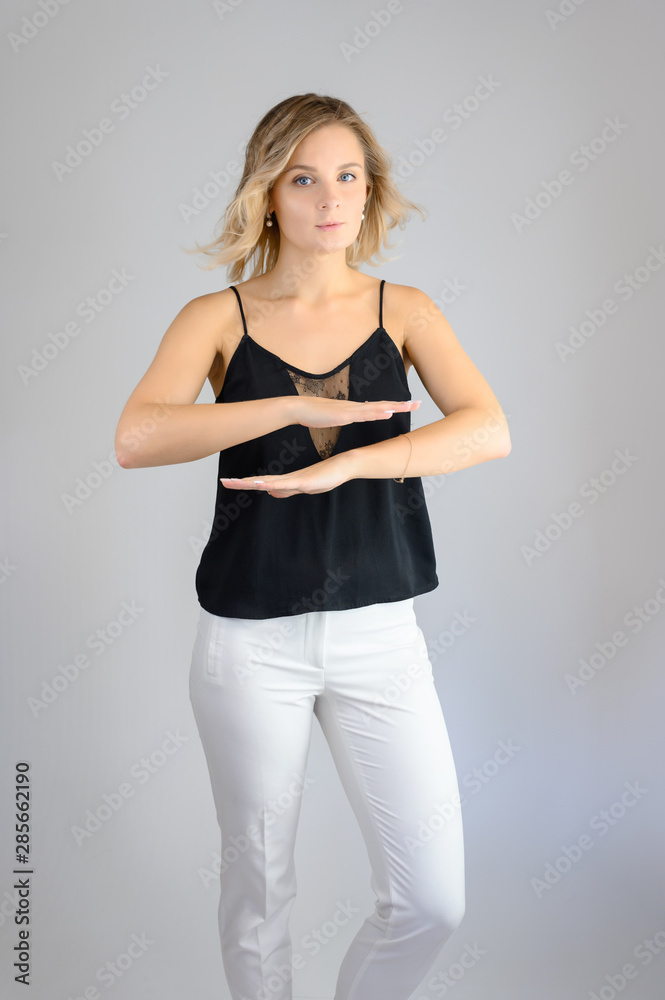 Full length studio portrait photo of a cute young blonde woman girl in a black blouse and white pants on a white background. He stands right in front of the camera, explains with emotion. Full length studio portrait photo of a cute young blonde woman girl in a black blouse and white pants on a white background. He stands right in front of the camera, explains with emotion.