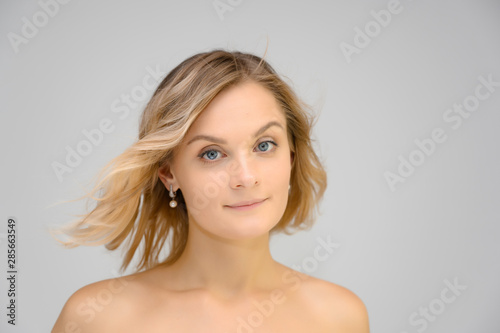 Closeup photo studio portrait of a fashionable pretty blonde young woman girl with beautiful hair on a white background. Standing right in front of the camera. Beauty, cosmetics.