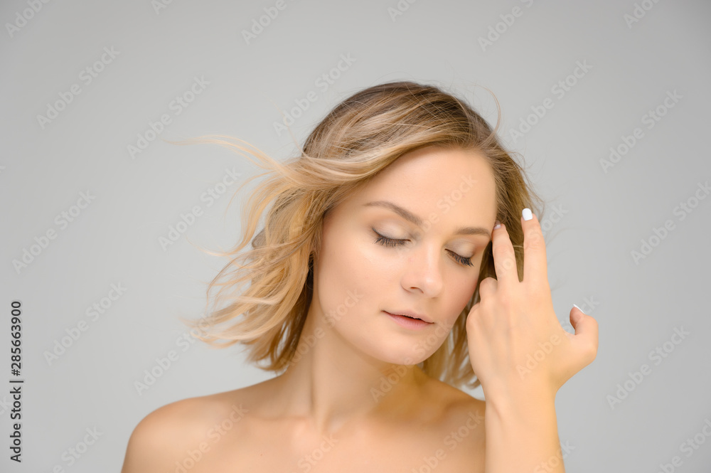 Closeup photo studio portrait of a fashionable pretty blonde young woman girl with beautiful hair on a white background. Standing right in front of the camera. Beauty, cosmetics. Closeup photo studio portrait of a fashionable pretty blonde young woman girl with beautiful hair on a white background. Standing right in front of the camera. Beauty, cosmetics.