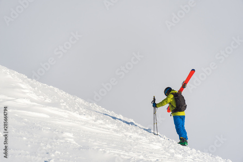Skier climbing a mountain on foot while carrying his skies ready for some off-piste. The overcast sky makes for a perfect neutral background with ample space for text