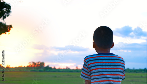 Back view of a young boy at the sunset and looking to the horizon.
