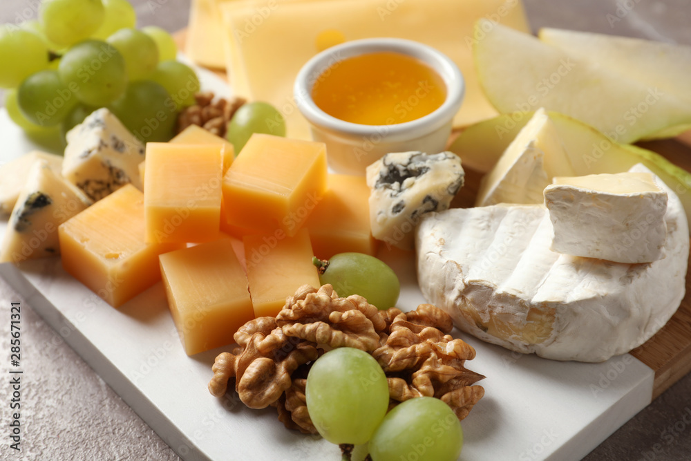Board with different kinds of delicious cheese and snacks on table, closeup