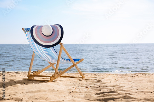 Fotografie Lounger and hat on sand near sea, space for text. Beach objects