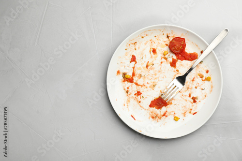 Dirty plate with food leftovers and fork on grey background, top view. Space for text photo