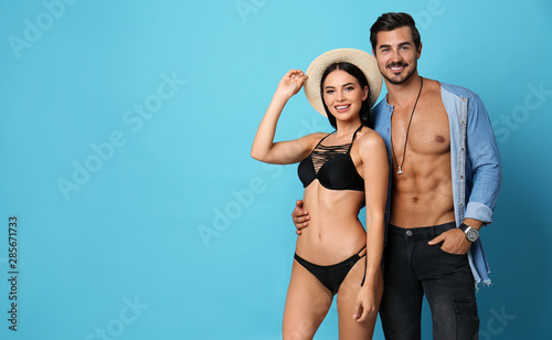 Beautiful young woman in stylish bikini and man on light blue background. Space for text
