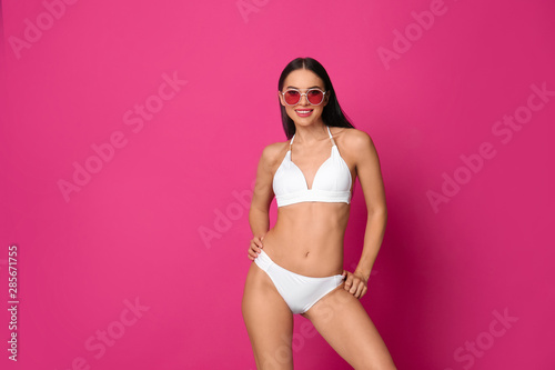 Beautiful young woman in white bikini with sunglasses on pink background. Space for text